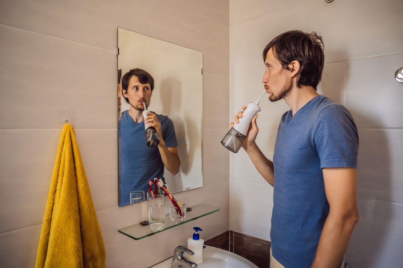 Man using portable water flosser in bathroom mirror, comparing water flosser versus traditional dental floss for plaque removal