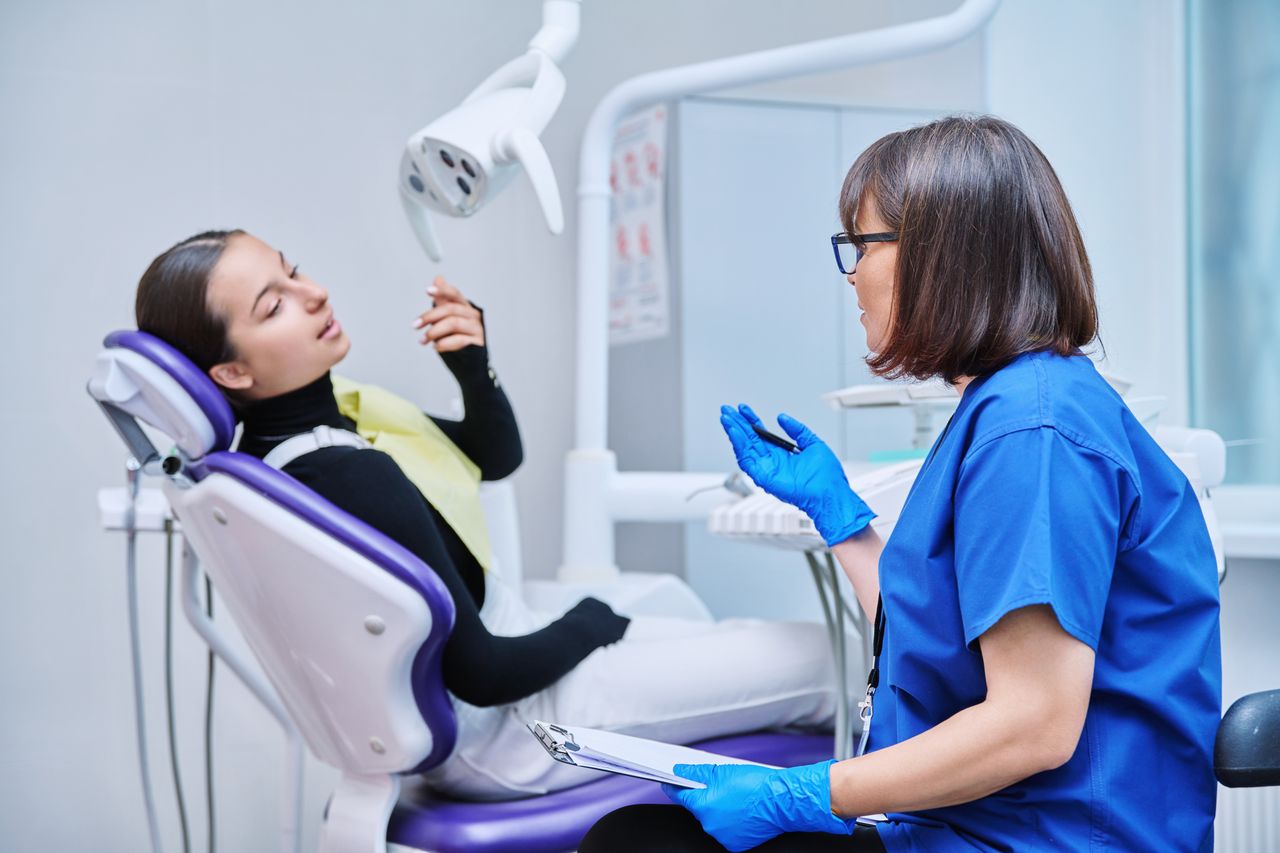 Pediatric dentist consulting with adolescent female patient during dental checkup