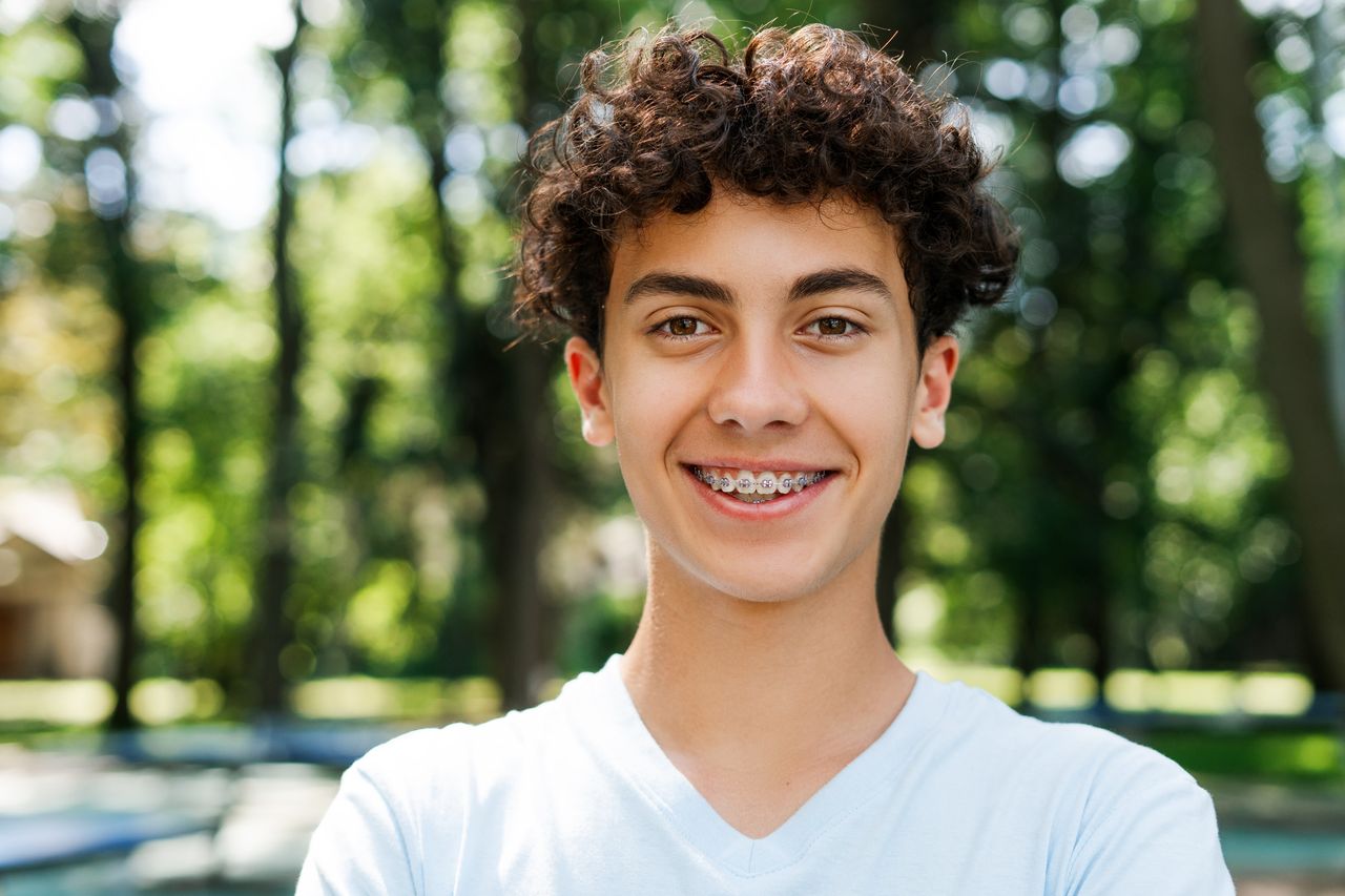 Happy teenage boy with braces smiling outdoors, showing healthy teeth after dental care