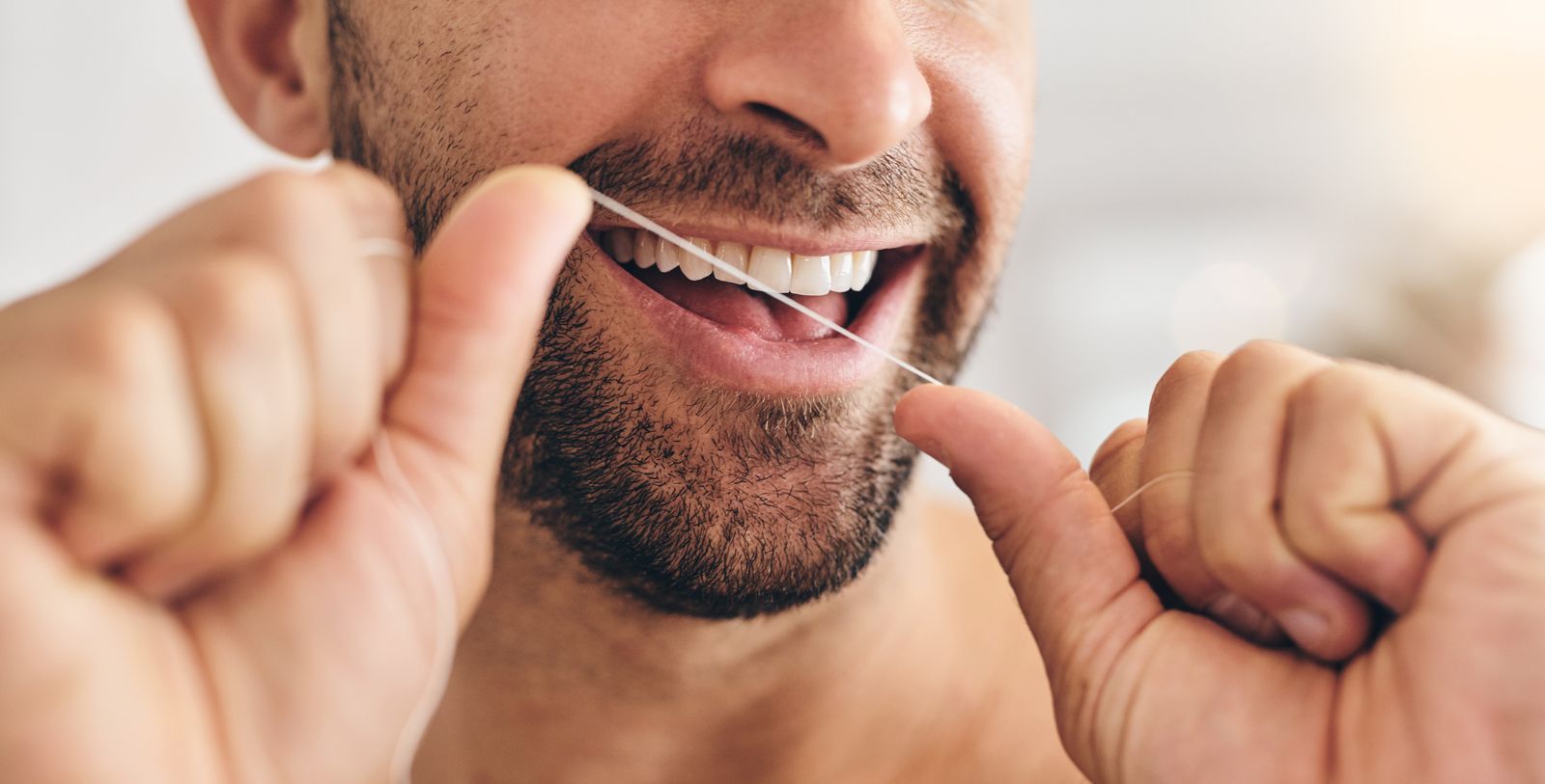 Close-up of a man flossing his teeth with traditional dental floss, showing proper interdental cleaning technique