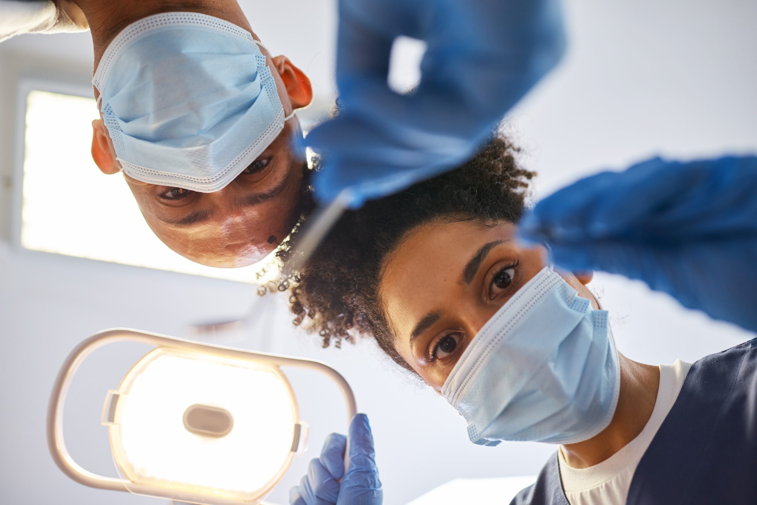 Two dentists in masks looking down at patient under exam light for emergency dental treatment at Dr. Foote Columbia MO