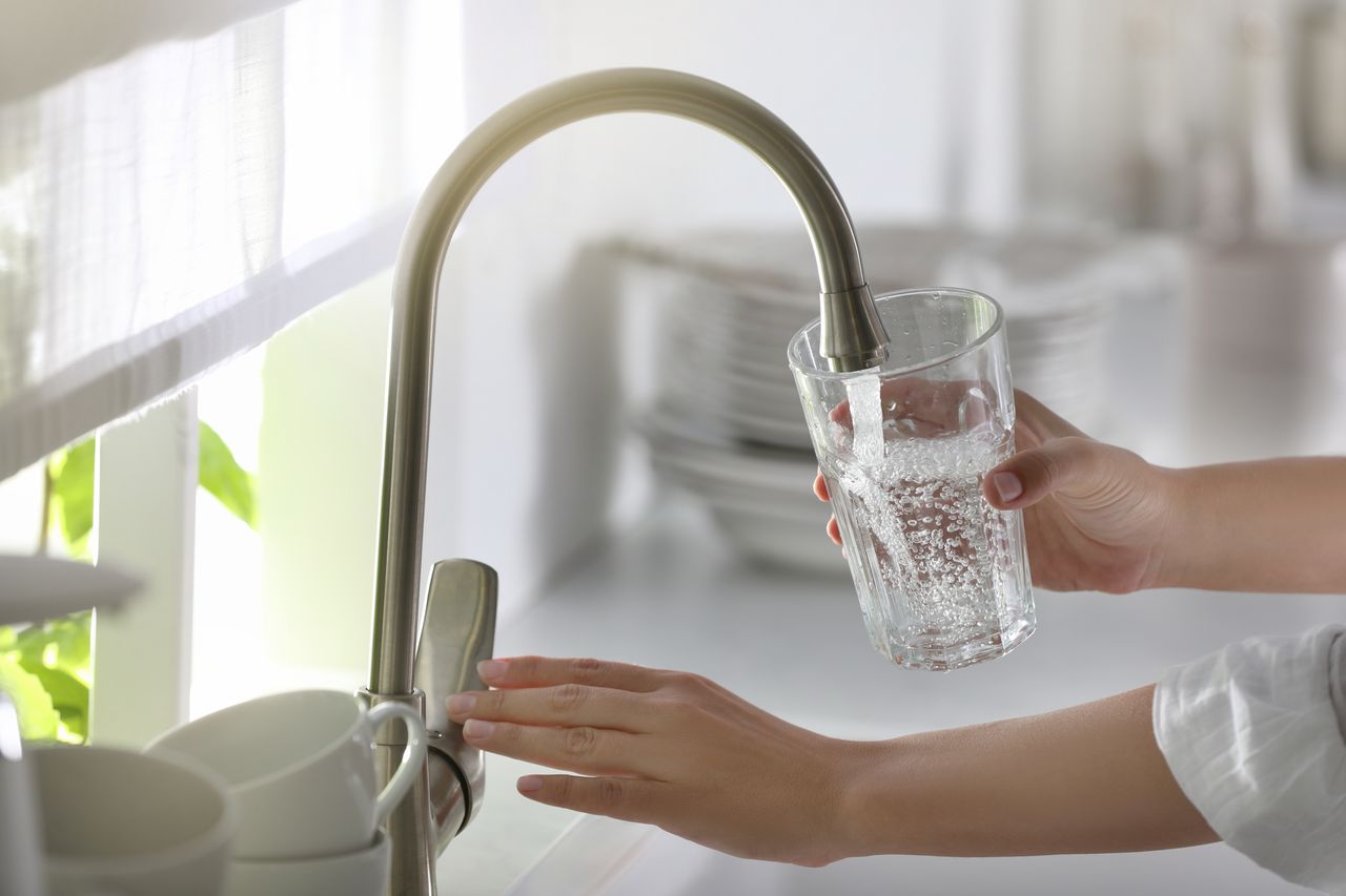 Person filling a glass of water from the kitchen tap, illustrating community water fluoridation and fluoride levels in public drinking water